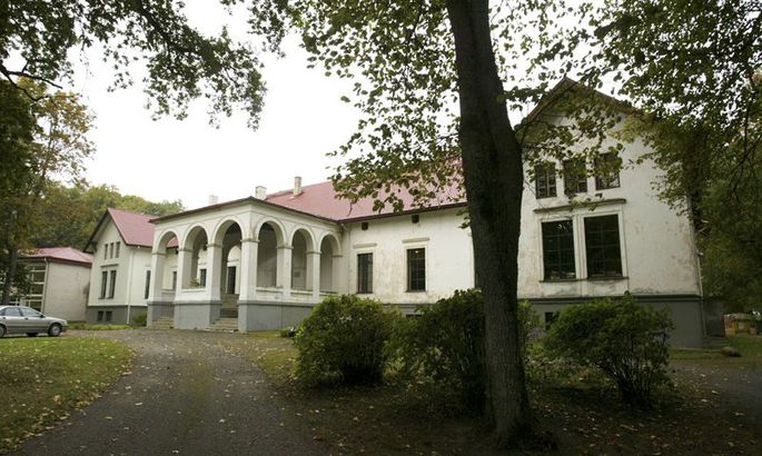 Pruuna mõisahoone vaade pargi poolt, ümbritsetud puudega.